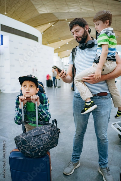 Obraz Father holding cute caucasian boy in airport. Child with suitcase and backpack waiting for delayed flight. Travelling with kids