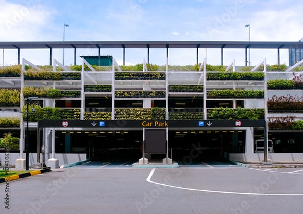 Fototapeta Exterior of modern multi-storey carpark building structure, with lush green plants on the facade - eco green wall. Architectural shot on bright sunny day. Front view. Green living plant wall