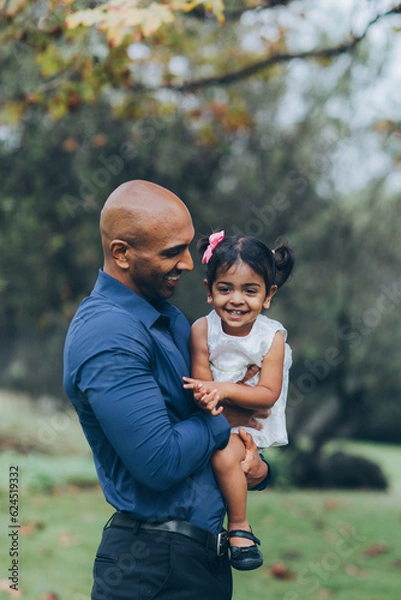 Obraz beautiful indian father playfully hugging his child daughter girl in the park with trees and greenery