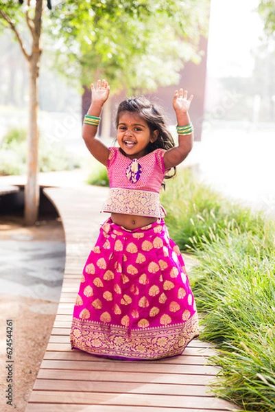 Obraz close up of little indian girl wearing a sari and bindi and traditional bracelets jewelry in front of trees and greenery