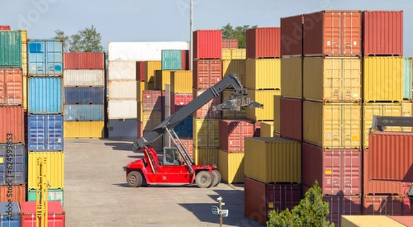 Fototapeta The red stacker stacks shipping containers at the port warehouse terminal