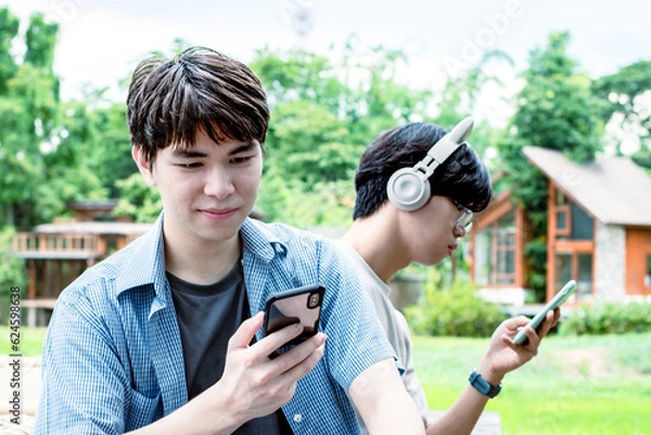 Fototapeta Portrait of young asian gay couple wearing headphones, sitting, listening to music and spending free time together in front of their house, good relationship, LGBT, and best friends concept.