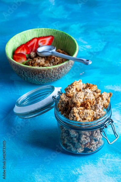 Obraz Healthy breakfast with granola and fresh strawberries served in a bowl on a blue background. Minimalistic composition with plate, spoon and natural morning light.