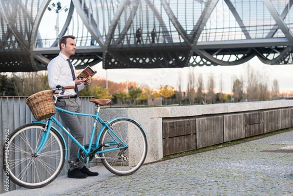 Fototapeta Business man with vintage bicycle by the river reading a book