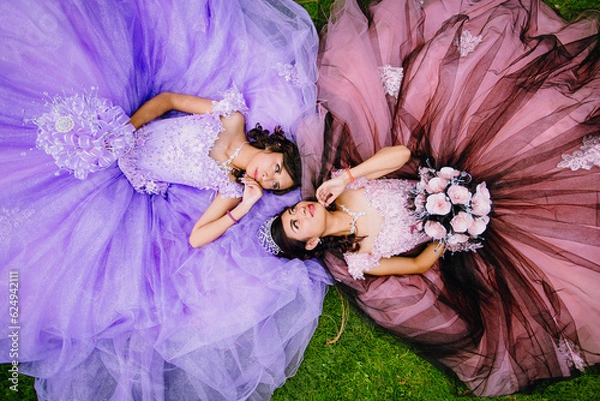 Obraz Portrait of Mexican quinceanera teenagers lying on the grass looking into each other's eyes