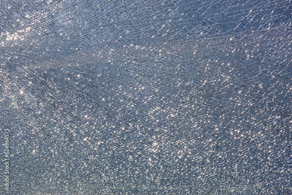 Obraz broken tempered glass in cracks, spoiled glass surface texture on blue sky background, shine from bright light, close-up.