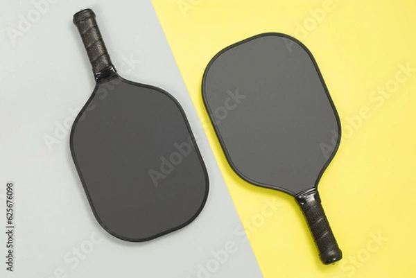Obraz Close top view of two black pickleball paddles on yellow and gray diagonal background. Sport game competition concept