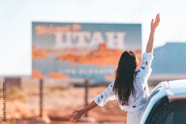 Fototapeta Beautiful woman on her trip by the car on the background of Welcome to Utah state border sign right in the Monument Valley