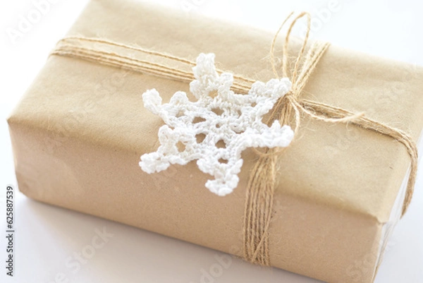 Fototapeta Christmas and New Year background. Gift box wrapped in kraft paper with jute cord. Decorated with a crocheted snowflake