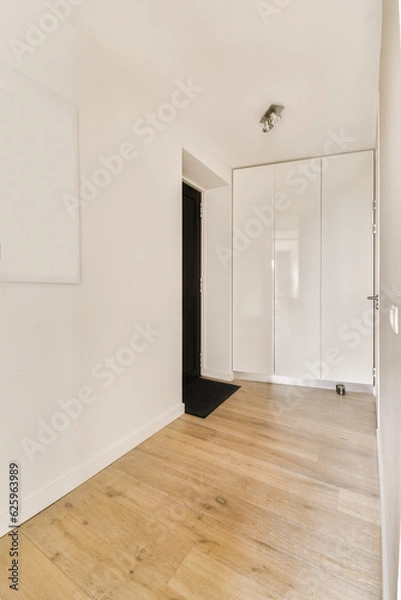 Fototapeta an empty room with white walls and wood flooring on the right, there is a black door to the left