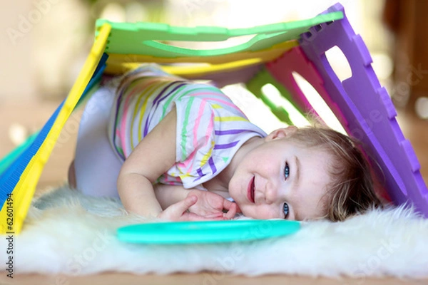 Fototapeta Happy little toddler girl playing hide and seek with puzzles