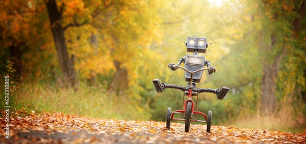 Obraz Szczęśliwego humanoidalnego robota jeździ na rowerze wzdłuż jesiennej uliczki. Obiekt robotyczny doświadcza uczuć i emocji. Koncepcja rozwoju technologii w postaci sztucznej inteligencji.