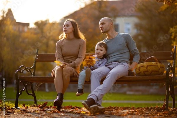Fototapeta Woman is sad on a bench next to her husband and son on an autumn day in the park