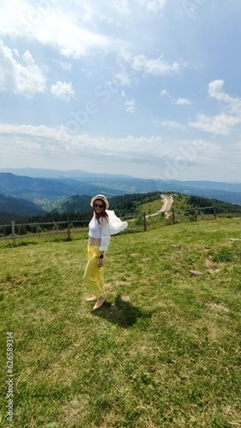 Fototapeta Traveling in summer Ukraine. Trip to Carpathian mountains. Woman tourist relaxing in flowers admiring view