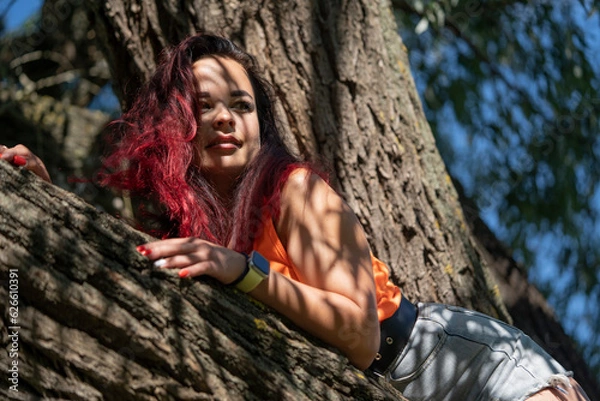 Obraz Portrait of a girl on a tree in a city park in summer