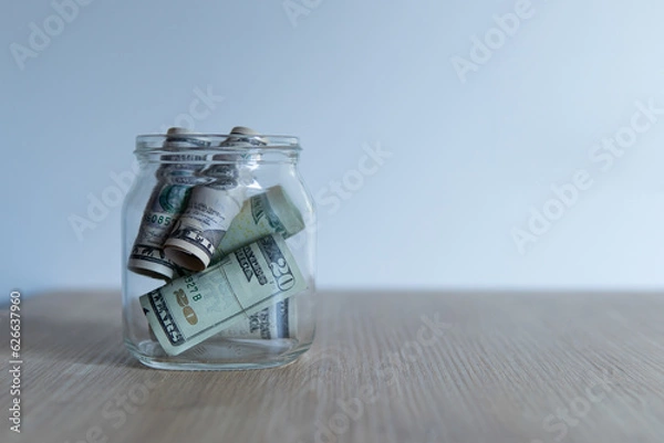Fototapeta money storage. open transparent jar with dollars inside on a wooden table.