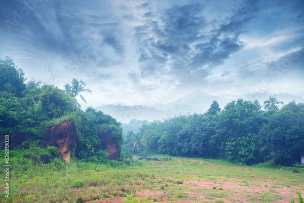 Obraz Landscape photography- A hillside full of green under a cloudy sky. In the distance, you can see breathtaking mountains