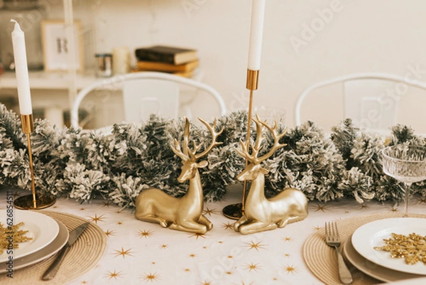 Fototapeta table set for Christmas or New Year's dinner with candles, ornaments, tablecloth and napkins on background of Christmas tree in loft style apartment