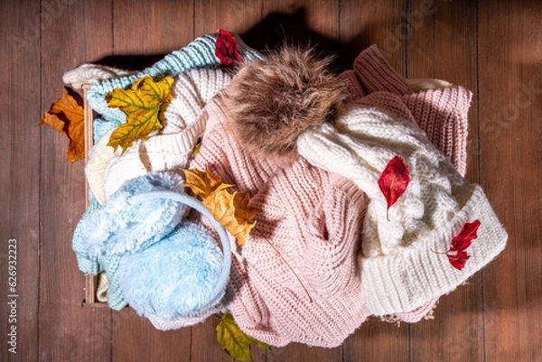 Fototapeta Preparation for fall and winter season, autumn warm cozy clothes, Stack of clean freshly laundered, neatly folded jackets, sweaters, blankets, hats, mittens in wooden box, taken from the mezzanine