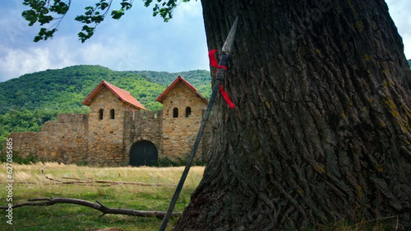 Fototapeta Roman fort and a spear leaning on an old tree in a summer day.