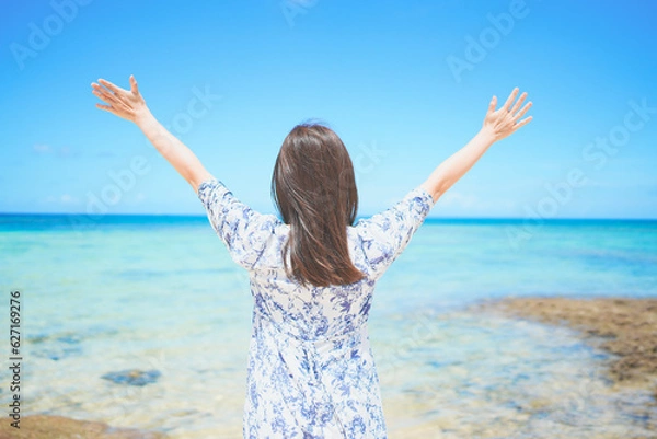 Obraz 沖縄のビーチで波風を感じる女性の後ろ姿