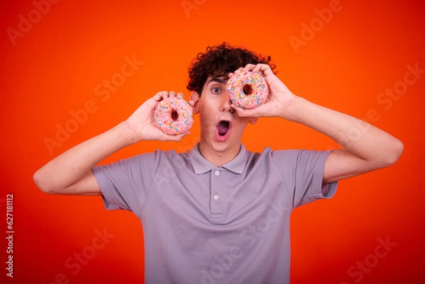 Fototapeta Young attractive guy eats pink donuts. Delicious breakfast and good vibes.