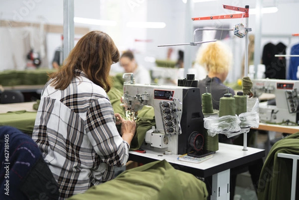 Obraz workers in an industrial garment factory sew clothes on sewing machine