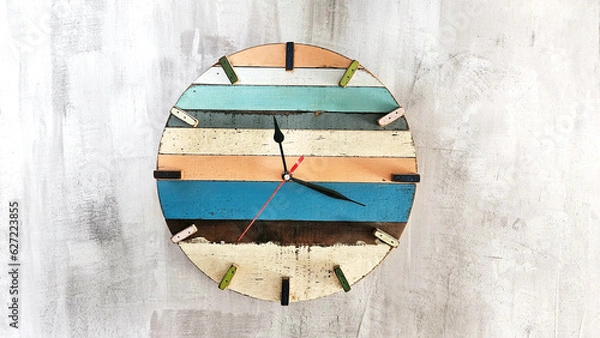 Fototapeta Wooden wall clock with a round dial and arrows, different colors on a plastered concrete wall