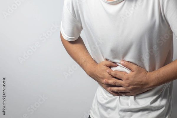 Obraz The man is holding his stomach with his hand against the white background, indicating that he has stomach pain.