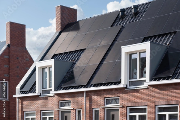 Fototapeta Solar panels mounted on the roofs of a row modern new-build social rental houses in Lemmer, Friesland, the Netherlands with blue sky