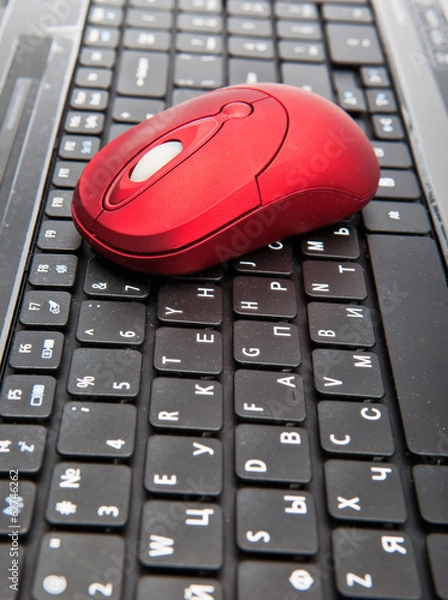 Obraz The red computer mouse on the black keyboard..