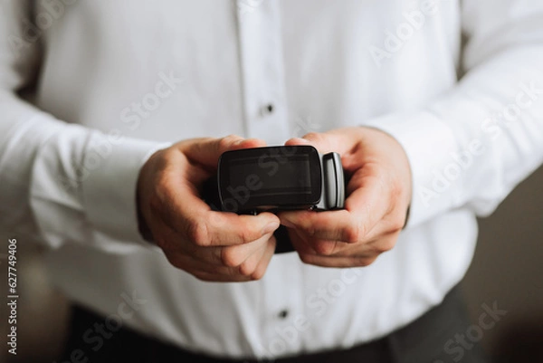 Fototapeta a man holds a black belt in his hands, close-up photo. The groom is preparing for the wedding ceremony