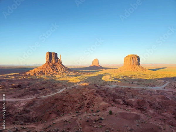 Fototapeta View of Monument Valley's 3 monoliths during sunset, with blue sky without any clouds. Reddish and orange colors