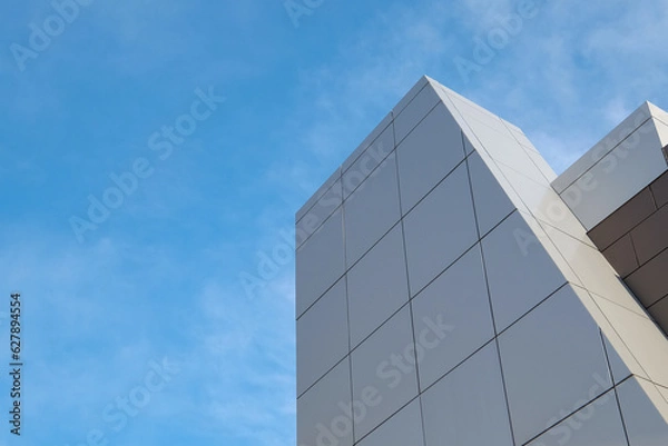 Fototapeta The exterior wall of a contemporary commercial style building with aluminum metal composite panels in various shapes. The futuristic building has engineered diagonal cladding steel frame panels. 