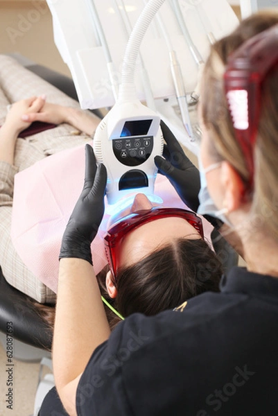 Fototapeta Close-up portrait of a female patient at dentist in the clinic. Teeth whitening procedure with ultraviolet light UV lamp