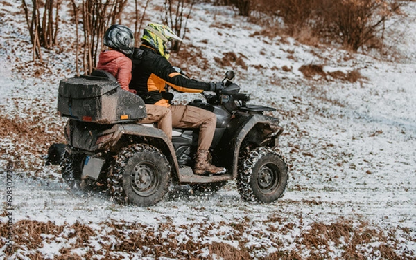 Fototapeta A young adventurous couple embraces the joy of love and thrill as they ride an ATV Quad through the snowy mountainous terrain