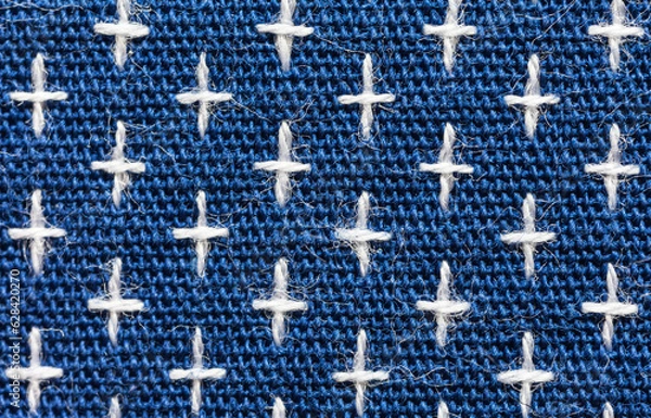 Fototapeta Close-up of machine embroidery sashiko with white crosses on blue background. Textile backdrop made of weaving natural cotton threads. Basis for sewing comfortable clothes, shirts, blouses. Macro