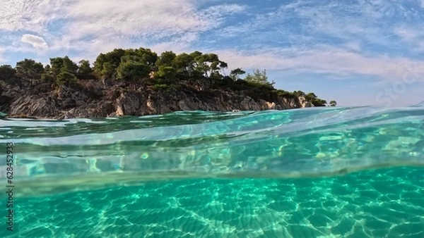Obraz Crystal clear sea water in Sitonia, Halkidiki, Greece. Shot from border of air and water with dome. Half underwater slow-motion view of sandy beach bottom and rock with trees