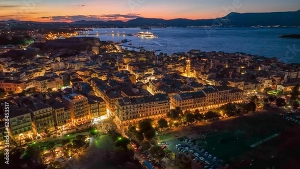 Obraz Old town with illumination against background of red sunset sky in Kerkyra, Corfu island. Evening aerial sunset view of Kerkyra, capital of Corfu island, Greece. 4K HDR shot