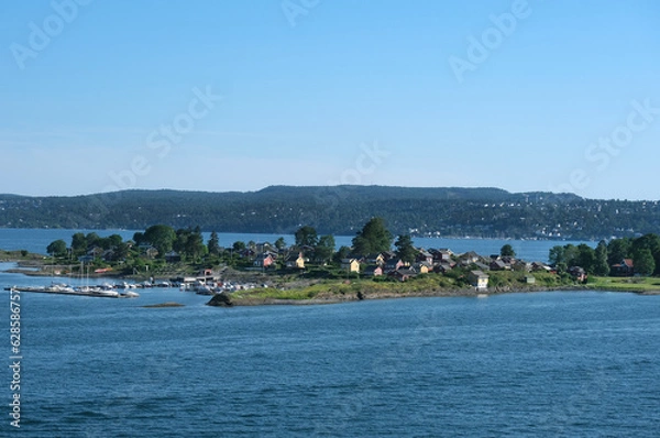 Fototapeta Norwegen im Sommer: Impression eines kleines Hafens und landestypischer Gebäude und Ferienhäuser auf einer Insel im Oslofjord, in der Nähe der norwegischen Hauptstadt Oslo, blauer Himmel
