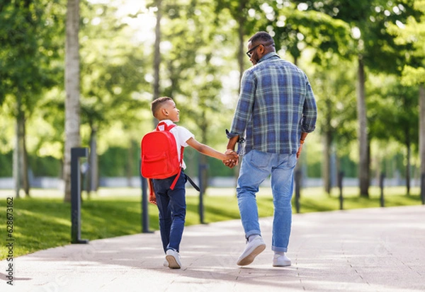 Fototapeta Schoolboy looking at father with smile while going with dad to first grade in school on sunny autumn day
