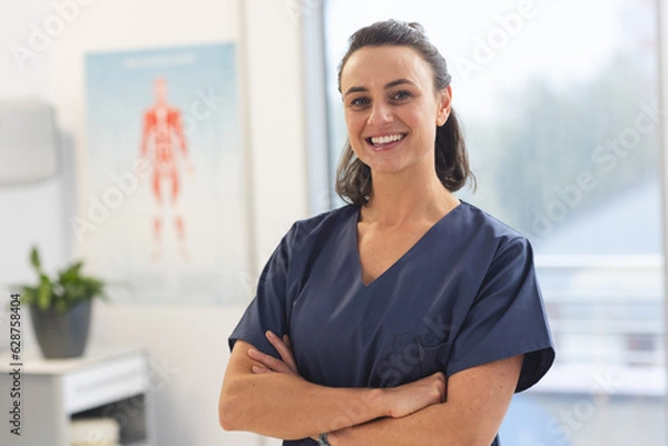 Fototapeta Portrait of happy female caucasian physiotherapist wearing scrubs at hospital
