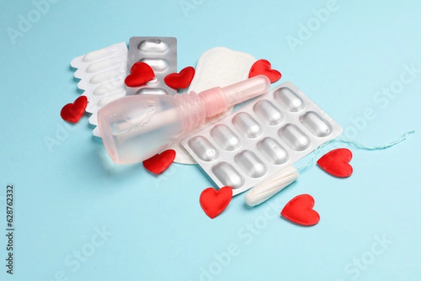 Fototapeta Women's health concept. Vaginal enema, Pad, tampon and pink awareness ribbon, pills, red hearts on blue background.