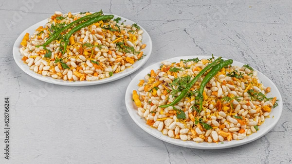Fototapeta Bhelpuri is a savoury snack or chaat. It is made out of puffed rice, vegetables, tangy tamarind sauce, sukhi bhel in white plate with chilies garnished