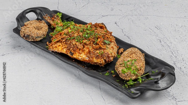 Fototapeta Pomfret fish tawa fry garnished with lemon and onion in a black ceramic plate with marble background,selective focus