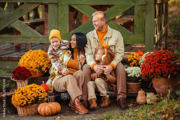 Obraz family traditions. multiethnic family i am in autumn in the park in a wooden gazebo next to pumpkins and flowers