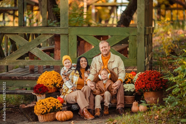 Obraz family traditions. multiethnic family i am in autumn in the park in a wooden gazebo next to pumpkins and flowers