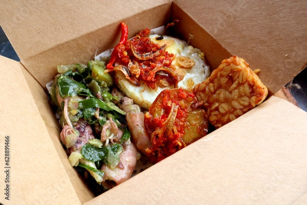 Fototapeta Rice bowl with spicy squid, fried tempeh, fried egg and chili sauce in a paper bowl