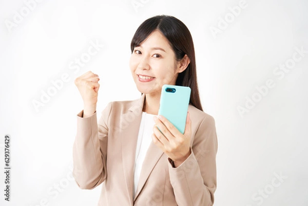Fototapeta スマートフォンを持ってガッツポーズをするミドルエイジのビジネスウーマン　白背景