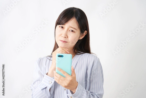 Fototapeta スマートフォンを持って悩むミドルエイジの女性　カメラ目線